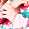 Close up sur les mains d'une femme qui porte un pull floral et des manchettes en tissu à rayures roses pour le petit je ne sais quoi
