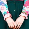 Une femme en jupe vert sapin et pull floral porte des manchettes en tissu à rayures roses claires pour le petit je ne sais quoi